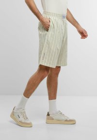 Des shorts rayés vert clair et blancs avec une taille élastique, des poches latérales et une coupe décontractée, associés à des baskets blanches et des chaussettes côtelées.