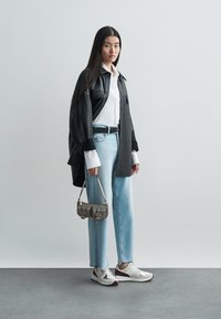 Black oversized shirt, white button-up shirt, light blue jeans, and gray/purple sneakers. Small metallic handbag with buckles.