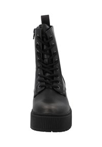 Botín negro de tobillo hecho de cuero suave, con un cierre frontal de cremallera, detalles de cordones, suela de goma texturizada y costuras decorativas.