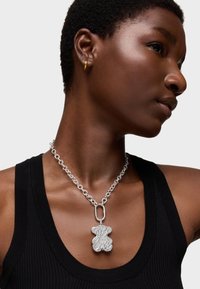 Pendentif en argent en forme d'ours sur une chaîne épaisse, porté sur un débardeur noir à côtes, mettant en valeur une surface texturée et un design à maillons.