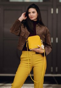 Žlutá kožená kabelka přes rameno s hladkou texturou, zaobleným tvarem, odnímatelným popruhem a dekorativním bílým květinovým doplňkem.