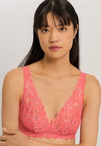 Krajkový bralet v jasně korálové barvě má hluboký V-výstřih, široké ramínka, květinový vzor a jemnou, poloprůhlednou strukturu.