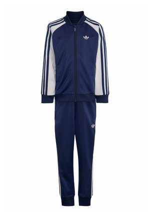 Granatowo-biały dres Adidas z kurtką na zamek, trzema białymi paskami na rękawach i spodniach oraz logo Adidas na klatce piersiowej i nodze.