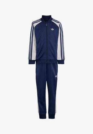 Mørkeblå og hvid Adidas træningsdragt med lynlåstrøje, tre hvide striber på ærmer og bukser samt Adidas-logo på bryst og ben.