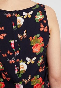 Top sin mangas con estampado floral que presenta un fondo azul marino con flores vibrantes y mariposas, detalles de botones en la parte posterior y una textura de tela suave.