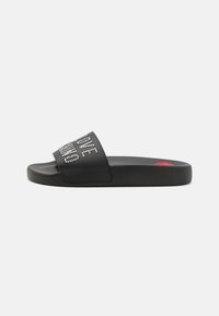 Black slide sandal with a textured surface, featuring a wide strap adorned with rhinestones spelling "LOVE." Red accent on the sole.