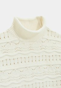Suéter de punto crema con cuello alto simulado, que presenta patrones texturizados y canalé vertical y horizontal en toda la prenda.