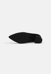 Chaussure en suédine noire à bout pointu, avec un petit talon bloc et une base texturée. Caractérisée par sa surface lisse et sa silhouette élégante.