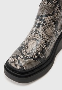 Snake-print ankle boot with a textured exterior, in shades of gray and black, featuring a rounded toe and a thick black sole.