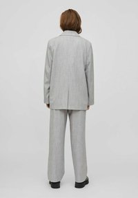 Grå skräddarsydd kostym med en lång, rak skärning av kavajen och vida byxor. Har en texturerad tyg och en klassisk slagdesign.