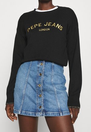 Henkilö pukeutuneena mustaan neuleeseen, jossa lukee kultaisella tekstillä "PEPE JEANS LONDON", ja etumuksin napitettavaan siniseen farkkujen minihameeseen.