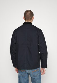 Dunkelblaues Jackett mit einem Cordkragen, gerader Schnitt und sichtbaren Nähdetails, kombiniert mit hellblauen Jeans.