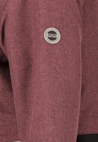 Maroon jakke med tekstureret stof, et rundt sølvfarvet "ZIGZAG" logo-patch og moderne snit.