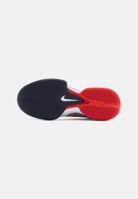 Semelle en caoutchouc noire et rouge d'une chaussure de sport avec une accroche texturée et un logo Nike Swoosh blanc au centre.