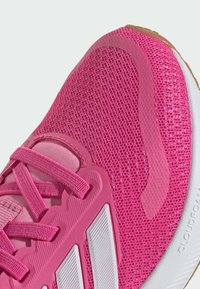 Chaussure de sport rose avec une tige en mesh, des lacets ton sur ton, un logo blanc et une semelle en caoutchouc texturée avec un design rembourré.