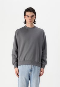Felpa grigia con colletto rotondo e polsini a coste, caratterizzata da un design semplice e una vestibilità comoda. Abbinata a jeans in denim blu chiaro.