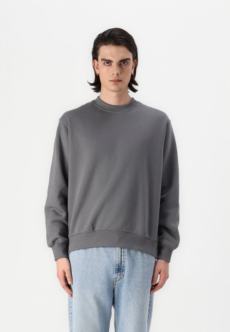 Felpa grigia con colletto rotondo e polsini a coste, caratterizzata da un design semplice e una vestibilità comoda. Abbinata a jeans in denim blu chiaro.