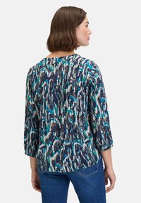 Blouse multicolore en bleu, vert et beige avec un motif brossé. Dispose de manches trois-quarts et d'un design plissé au dos.