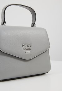 Szara skórzana torebka o usztywnionej konstrukcji, z zapięciem na klapę na magnes i srebrnym logo. Posiada krótki uchwyt i gładką fakturę.