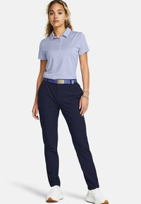 Lysblå polo t-shirt med korte ærmer og tre knapper, parret med marineblå bukser og et matchende bælte. Hvide sneakers fuldender outfittet.