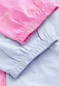 Lähikuva vaaleanpunaisesta kankaasta, jossa on hymyprintti, ja vaaleansinisestä kankaasta, molemmat elastisilla reunoilla, aseteltuina kerroksittain.