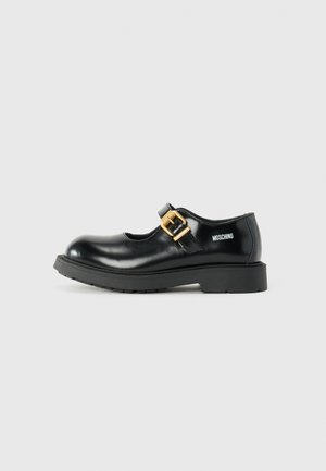 Zapatos Mary Jane de charol negro con punta redondeada, un acento de hebilla dorada y suela de goma negra gruesa. Logo de Moschino en el lateral.