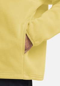 Giacca di felpa gialla con una texture morbida, tasca laterale e vestibilità rilassata con polsini e orlo a coste.