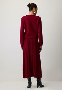Sukienka dzianinowa w głębokim czerwonym kolorze z prążkowaną fakturą, długimi rękawami i dopasowaną talią, w połączeniu z wysokimi czarnymi botkami.