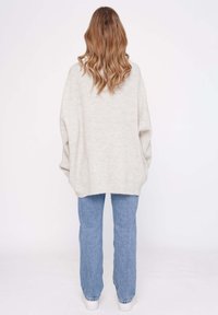 Kuscheliger, hellgrauer Strickpullover mit oversize Passform, kombiniert mit hellblauen Jeans und weißen Turnschuhen, von hinten betrachtet.