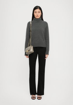 Woman wearing a gray turtleneck sweater, black flared pants, black open-toe heels, carrying a beige crossbody bag with a gold chain strap.