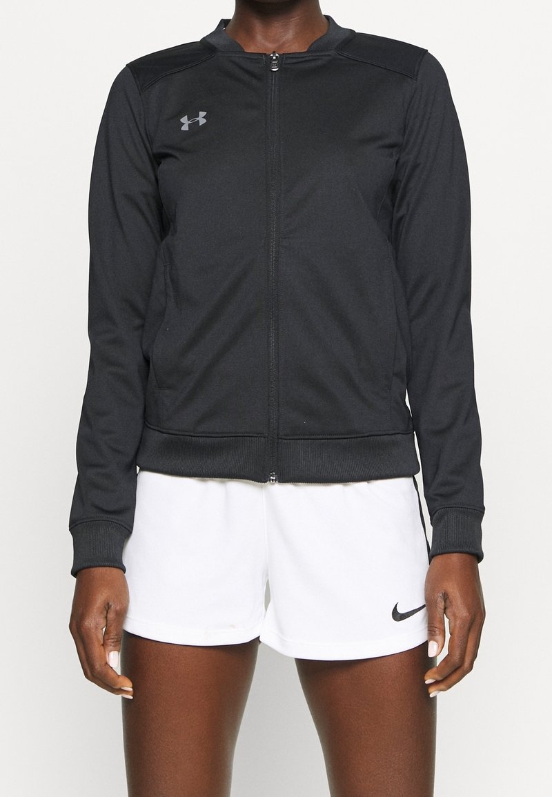 Black zip-up athletic jacket made of smooth fabric with long sleeves, ribbed cuffs, and a subtle logo on the chest. Paired with white shorts.