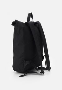 Mochila negra con un respaldo de malla texturizada, correas ajustables y un diseño simple y estructurado. Sin logotipos ni patrones visibles.