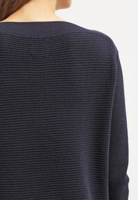 Pull en maille marine avec un motif côtelé texturé. Présente un large col et des manches longues, offrant une coupe décontractée.