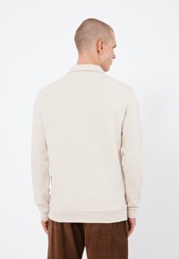 Pullover beige chiaro con colletto, maniche lunghe e polsini a coste. Realizzato in tessuto morbido, progettato per il comfort. Vista posteriore mostrata.