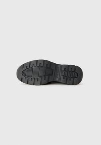 Suola di scarpa in gomma nera con un motivo a tramatura testurizzato, caratterizzata da linee e scanalature rialzate per una migliore aderenza e trazione.