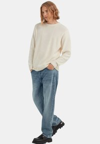 Ecru gebreide trui met een textuurpatroon, ronde halslijn, geribbelde manchetten, gecombineerd met lichtblauwe ruime jeans en zwarte chunky schoenen.