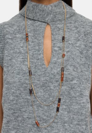 Złocony naszyjnik z dwoma rzędami, z naprzemiennie ułożonymi brązowymi i pomarańczowymi koralikami, uzupełniony szarym dzianym topem z dekoltem typu keyhole.