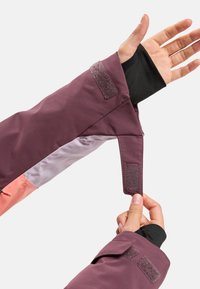 Maroon jacket sleeve with adjustable velcro strap, featuring contrasting pink and gray panel details, smooth texture, and secure closure.