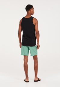 Canotta nera, pantaloni corti verde menta, infradito. Design semplice, materiale in cotone, vestibilità rilassata, e cuciture visibili sui pantaloni corti.
