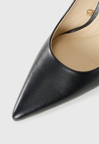 Black pointed-toe leather high heel shoe with beige interior lining on a white background.
