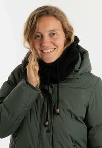 Groene pufferjas met een capuchon, voorzien van een zwarte gebreide sjaal, zwarte trekkoorden en houten accenten bij de sluitingen.