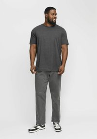 Camiseta de cuello redondo gris oscuro, de corte relajado, combinada con pantalones gris claro. Zapatillas deportivas en blanco y negro con un diseño deportivo. Un look simple y funcional.