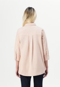 Camicia a maniche lunghe a strisce rosa chiaro, con colletto, dettaglio plissettato sul retro e polsini arrotolati. Abbinata a jeans scuri.