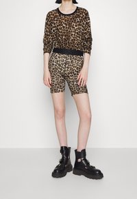 Długi rękaw t-shirt w leopardzie wzory z czarnym wykończeniem, w połączeniu z szortami rowerowymi w leopardzie wzory. Masywne czarne botki z paskami i teksturowaną podeszwą.