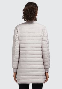 Jachetă lungă, quilted, de culoare gri deschis, cu cusături verticale, guler înalt și manșete ribbate. Prezintă un fermoar lateral și detalii minime de branding.