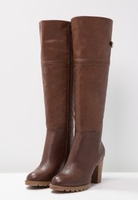 Botas altas de imitación cuero marrón con tacón cuadrado, detalles de costura sutiles y una cremallera lateral para un fácil uso. Suela texturizada para mayor agarre.
