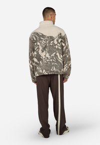 Fleece'owy pulower w kolorze kremowym i szarym, z teksturowanym, abstrakcyjnym wzorem, wysokim kołnierzem i luźnym krojem, zestawiony z ciemnymi spodniami z bocznymi paskami.