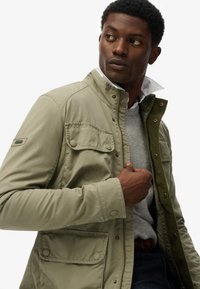 Lichtgroene, knoop-jack met een corduroy accent op de kraag, voorzakken en drukknoopsluitingen, gelaagd over een grijze trui.