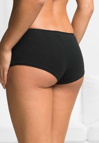 Boyshorts neri in cotone con una texture liscia, caratterizzati da un elastico in vita a bassa altezza e bordi senza cuciture, mostrati da una prospettiva posteriore.