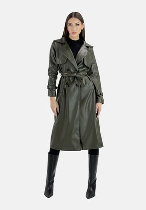 Trench coat in ecopelle verde oliva con bottoni doppi, ampie alette e vita con cintura, abbinato a stivali neri sopra il ginocchio.